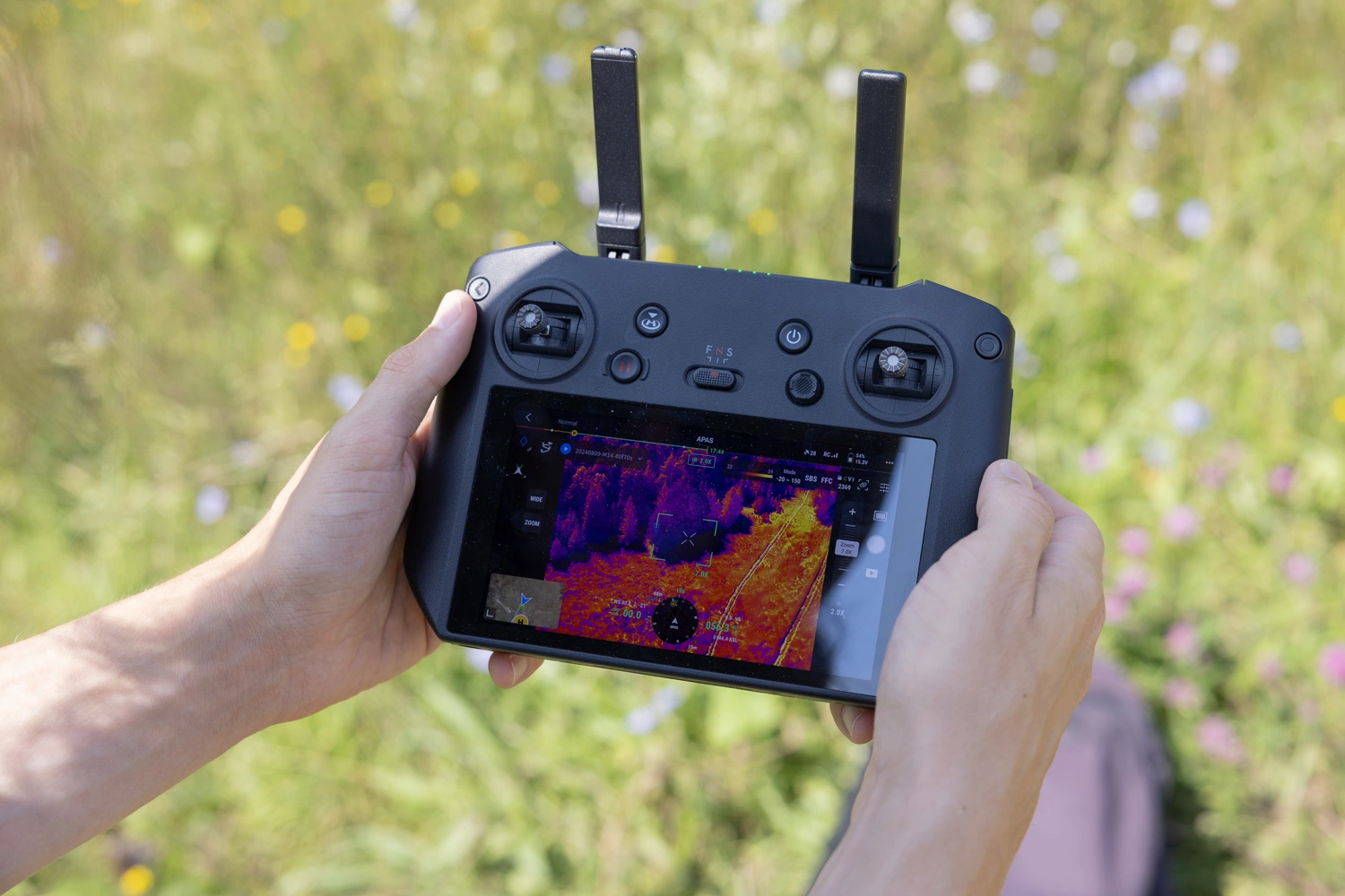 A pair of hands holding a drone remote with a monitor displaying thermal data in different colours