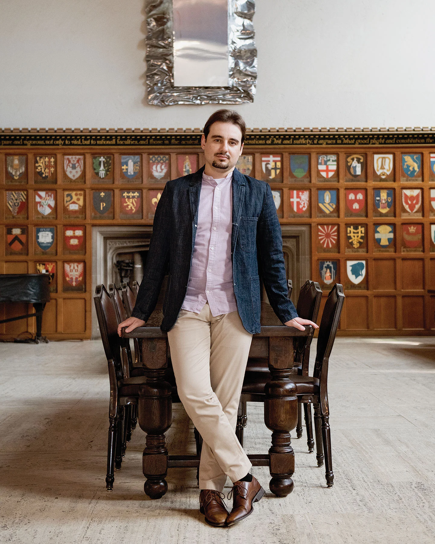 Vadym Lytvynov leaning against a long wooden table in a room with a wood-panelled wall decorated with coats of arms