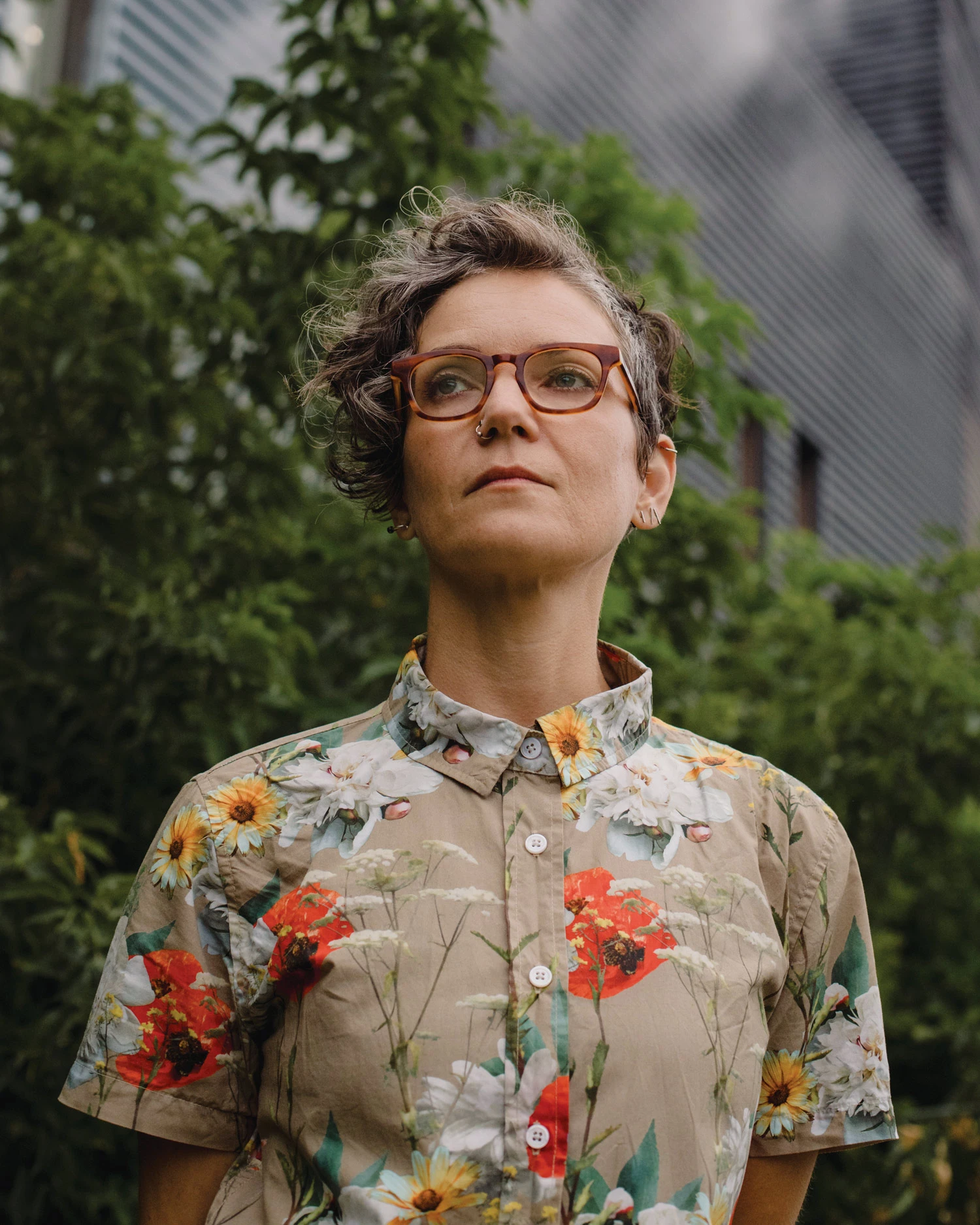 Outdoor shot of Zoë Wool, wearing a short-sleeved, button-up shirt with a print of large colourful flowers